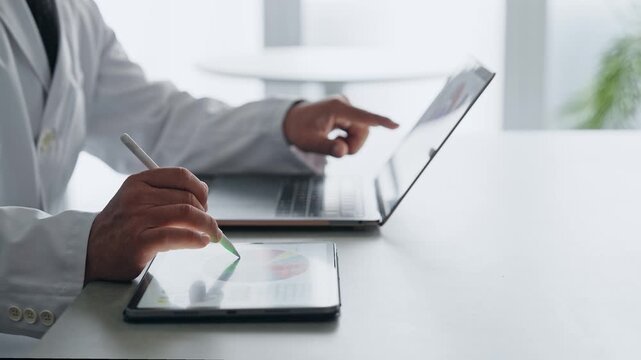 ノートパソコンとタブレットPCを使って作業する白衣の男性