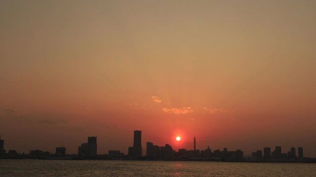 横浜ベイブリッジから見るオレンジ色に染まる「みなとみらい」のビル群のシルエットと太陽が沈む様子　夕景　タイムラプス