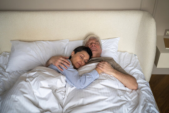 Trust, love and closeness in elderly relationships, senior man and woman embracing while sleeping, happy husband and wife hugging holding hands during night sleep, loving aged partners enjoying rest