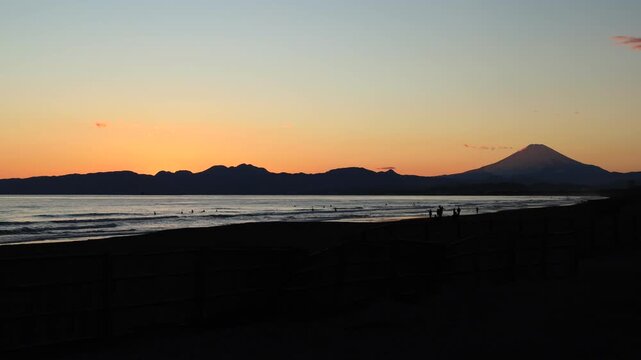鵠沼海岸にて、日没にサーフィンや散歩をする人と富士山のシルエット　夕景　タイムラプス