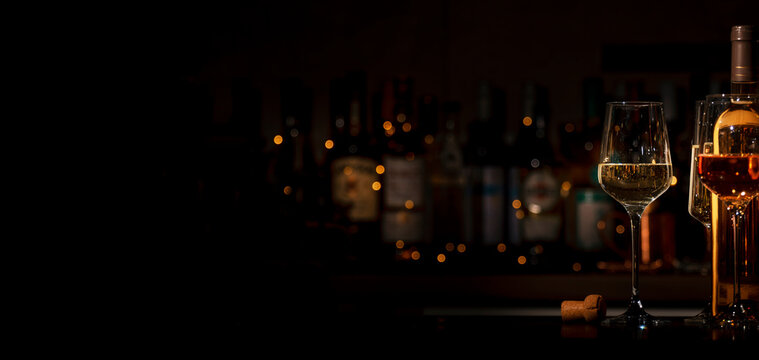 Glasses of white and rose wine on bar counter with blurred bottles and bokeh lights in background. Luxury degustation and evening relaxation concept.