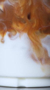 4K close-up of rich espresso swirling and mixing into fresh white milk in a glass, Abstract iced coffee latte texture beverage background, food styling concept.