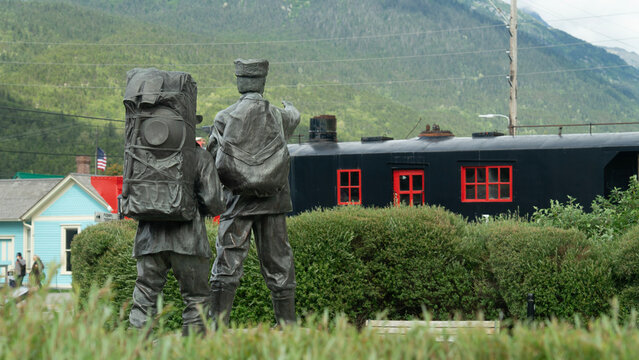 Bronze statue of Klondike gold rush pioneers with vintage train car in Skagway, Alaska.