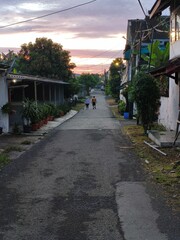 Fototapeta premium Quiet Residential Street at Dusk with People Walking in Distance, Indonesian Village Alley