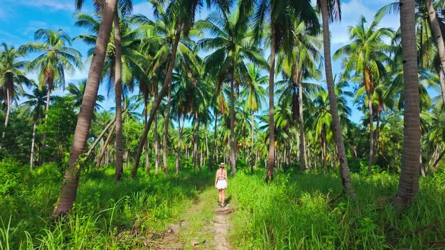 Young woman in white outfit strolls beneath lush coconut trees in paradise