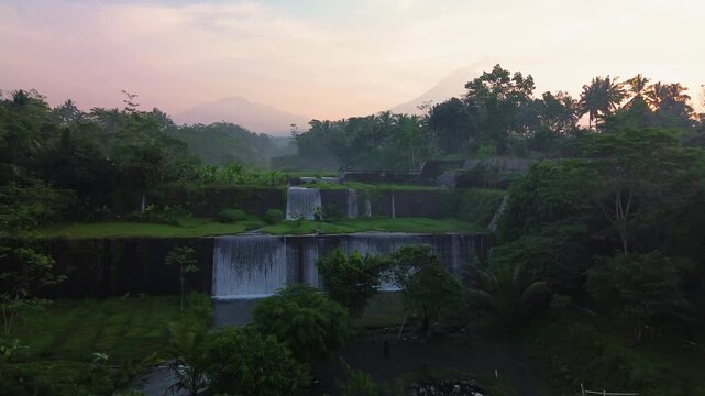 Aerial footage of the Sabo Dam area, which boasts a strong water flow in the morning. 4K drone footage of the Sabo Dam area surrounded by green grass and mountains in the background at sunrise.