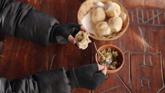 Gloved hands spread jam onto freshly baked rolls at a wooden table, creating a cozy, tactile experience. Perfect for culinary blogs or winter-themed content.