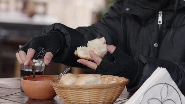 A person wearing gloves spreads jam on freshly baked bread at an outdoor table. Ideal for use in food blogs or culinary content.