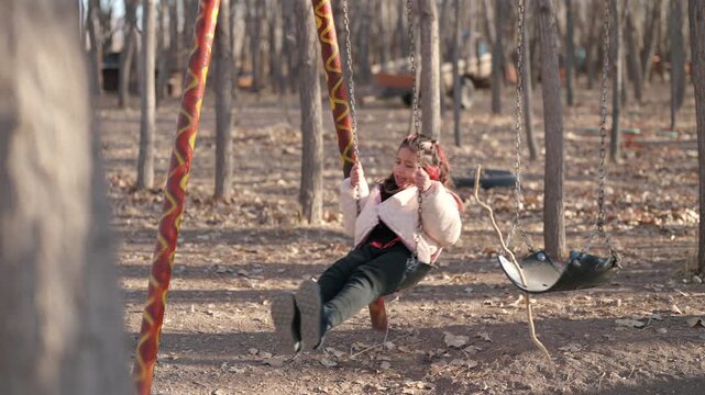 Girl swinging in a park with a forest backdrop and soft blurred foreground.