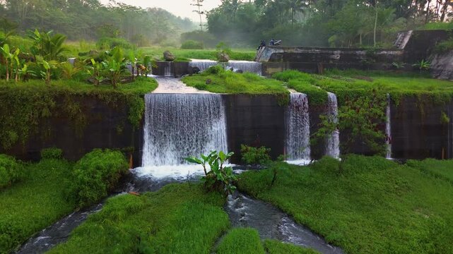 Aerial footage of the Sabo Dam area, which boasts a strong water flow in the morning. 4K drone footage of the Sabo Dam area surrounded by green grass and mountains in the background at sunrise.