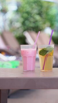 Side view of three colorful cold drinks with straws on poolside table at sunny tropical resort. Vertical reel of refreshing summer beverage and vacation lifestyle concept with soft blurred background