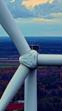 Large wind turbine rotor slowly turning above autumn forest and open landscape