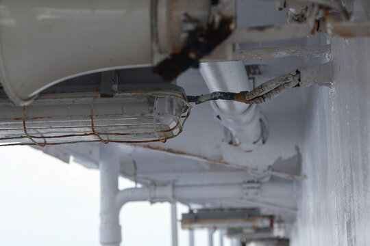 a weathered industrial light fixture with exposed wiring, protective metal guard, rust, and painted structural elements