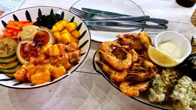 Closeup of assorted seafood platter and poke bowl on white wooden table in restaurant