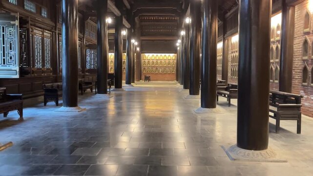 Reveal shot inside Bai Dinh Pagoda in Ninh Binh Vietnam featuring dark wooden pillars, brick walls with Buddha niches and benches along temple hall