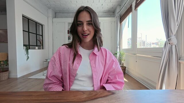 Confident female influencer vlogging from her modern apartment, actively speaking and gesturing during a video call while engaging with her audience from a point-of-view perspective