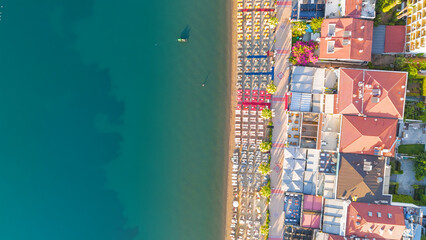 Fototapeta premium Marmaris, Turkey. Commercial top-down view of beachfront with geometrically aligned umbrellas, promenade and hotels. Morning light on calm sea with gentle waves.. Aerial View