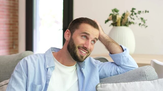 Handsome young caucasian man relaxing on the sofa at home, looking away with a gentle smile and daydreaming about his future. Peaceful and contented guy feeling happy and satisfied