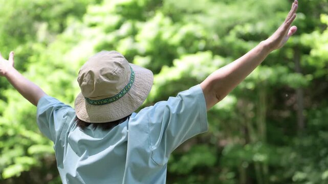 森林浴を楽しみながら深呼吸で両手を広げる女性　アウトドアや夏のキャンプを楽しむ顔無しの後姿イメージの動画