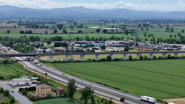 A1 Autostrada del Sole, Autogrill service area, A21 motorway corridor, and SS9 Via Emilia cross the Po Valley near Fiorenzuola d&rsquo;Arda exit, Piacenza Emilia Romagna, Italy, aerial establishing shot