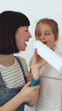 A mother and her young daughter share a joyful moment while holding a paint roller, preparing to redecorate their home