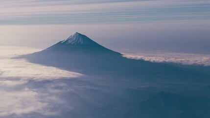Fototapeta premium Symmetrical volcanic mountain peak rising above a soft cloud layer for mountain travel, nature landscape advertising and environmental conservation concepts