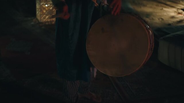 Traditional Berber bendir frame drum with animal skin membrane being played at a desert campfire night in Morocco