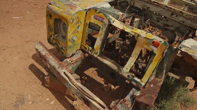 Close up of a crushed yellow rally car chassis with peeling paint rust and stickers abandoned in the Sahara Morocco