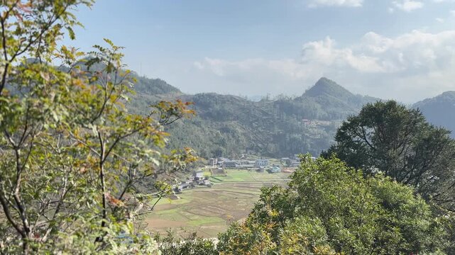 View from Lung Cu Flag Tower stone steps through green forest toward patchwork farmland valley and limestone mountains in Dong Van Karst Plateau Geopark