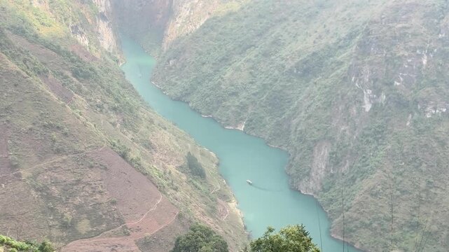 High angle view of turquoise Nho Que River winding through steep canyon walls with small boat crossing Tu San Canyon in Ha Giang Vietnam