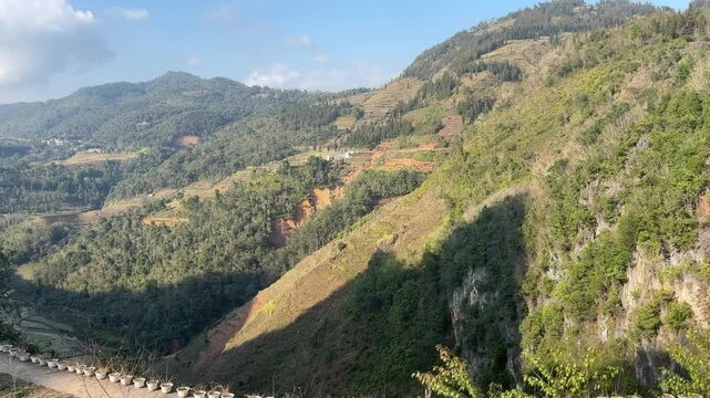 High angle view of lush terraced mountain slopes and small valley beneath bright partly cloudy sky in Dong Van Karst Plateau Ha Giang Vietnam