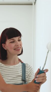 A mother and her young daughter are painting a white wall together with a roller, enjoying a home renovation project