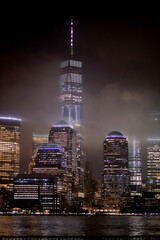 Fototapeta premium Serene Night Scene Of Towering Buildings Glowing Amidst Drifting Fog Over River new york