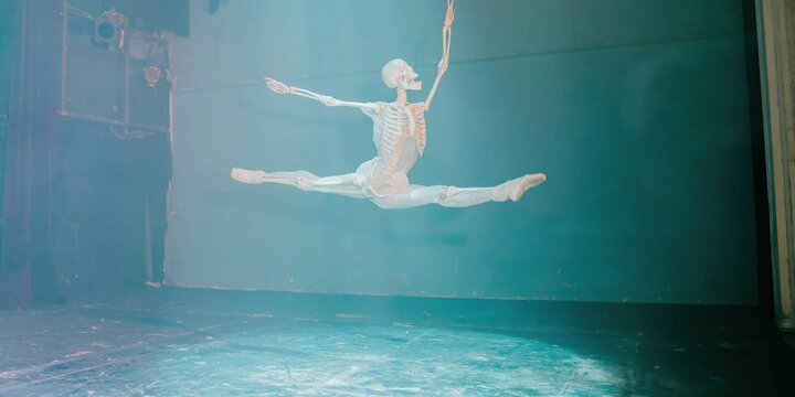 Human skeleton performing a ballet jump across a dark theatre stage for theatrical production, dance event promotions and artistic halloween advertising