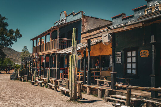 Perspective view of a desert dirt street with wooden storefronts and cactus in wild west style