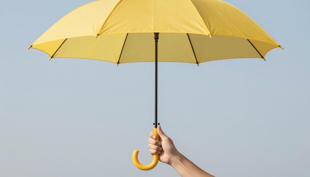 Hand holding open yellow umbrella against a pale blue sky, minimalist protective accessory