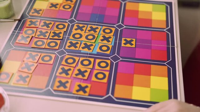 child's hand placing tile with X onto colorful board during game tic tac toe, Fine motor skills practice, detailed shot focusing on move and interaction, puzzle solving, Strategic thinking for kids