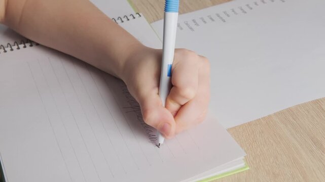 left-handed schoolchild doing homework, child writes English in notebook, assignments involving English language exercises, acquisition, vocabulary building in school setting, Bilingual Education
