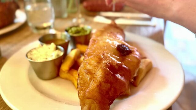person squeezing lemon onto battered fish and chips with condiments on plate