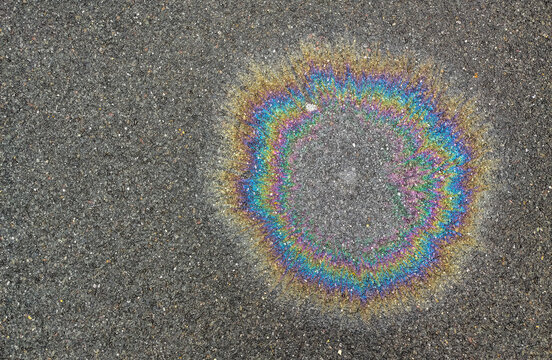 Rainbow oil slick on wet asphalt texture background showing colorful gasoline spill on dark pavement
