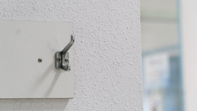 Close-up of a metal wall hook mounted on a textured white wall with a blurred background.