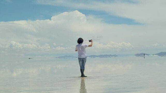 A very photogenic man from Bolivia taking a selfie with the Uyuni Salt Flat in the background - concept of tourism