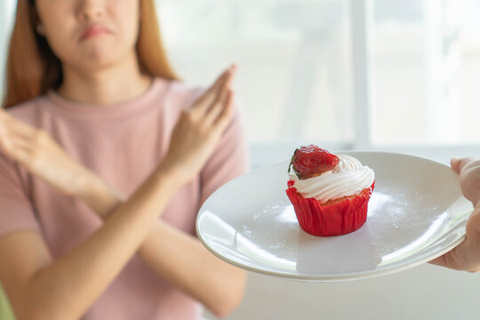 Woman on dieting for good health concept. Woman doing cross arms sign to refuse sweet cupcake
