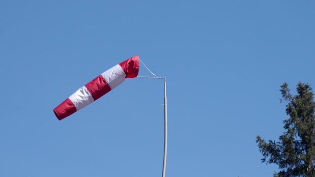 Red and white windsock blows in the wind against clear blue sky. Concept of weather, wind direction and outdoor conditions.