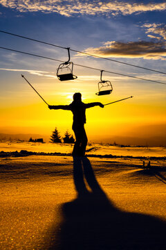 Silhouette of a skier enjoying a sunset on a snowy mountain with chairlifts in the background