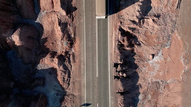 Top down ascending spiral over truck driving along highway squeezed between dramatic eroded salt rock canyon walls casting sharp shadows. Valle de la Muerte, Chile