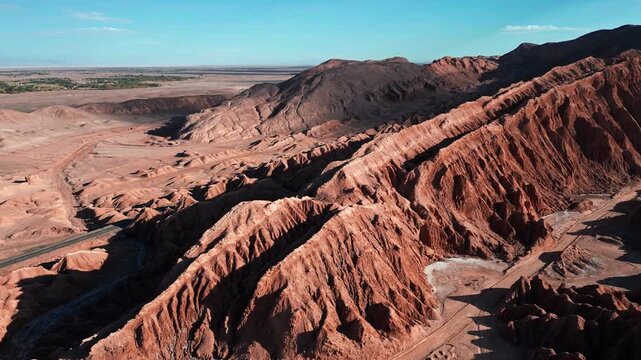 Orbit over dramatic eroded salt rock ridges and ravines of the Cordillera de la Sal with San Pedro de Atacama oasis visible in the distant plain. Valle de la Muerte, Chile