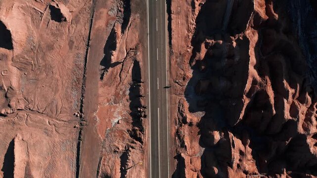 Top down view of straight highway cutting between dramatic eroded salt rock canyon walls casting deep shadows on both sides. Valle de la Muerte, Chile