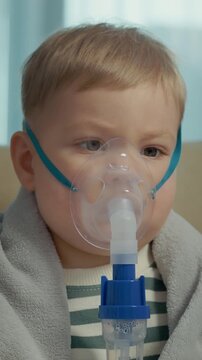 Vertical Screen: A child is receiving treatment with a nebulizer mask to help with cough and respiratory infection at home. The child breathes in the saline solution for relief.