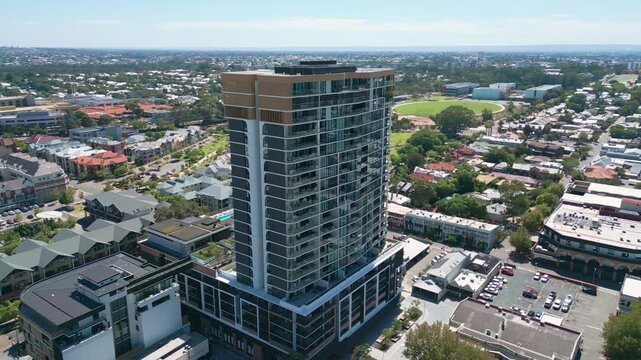 Orbit shot around modern high rise residential tower with glass facade revealing low density suburban sprawl sports oval and tree lined streets in all directions. Subiaco, Perth, Australia
